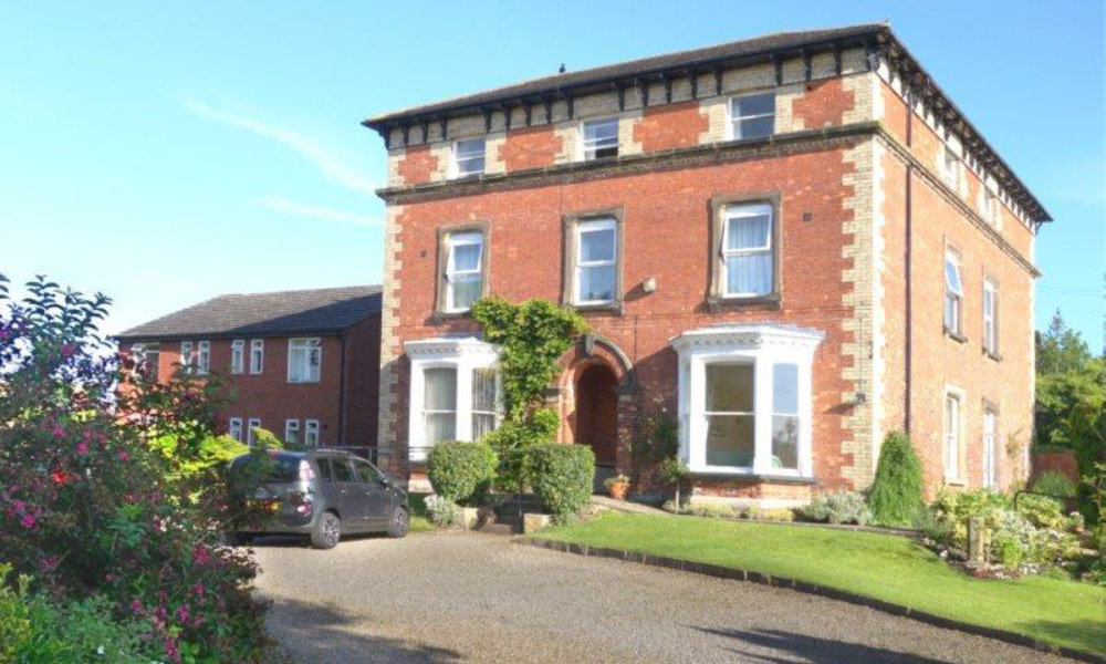 Photo of large brick house with big bay windows surrounded by gardens