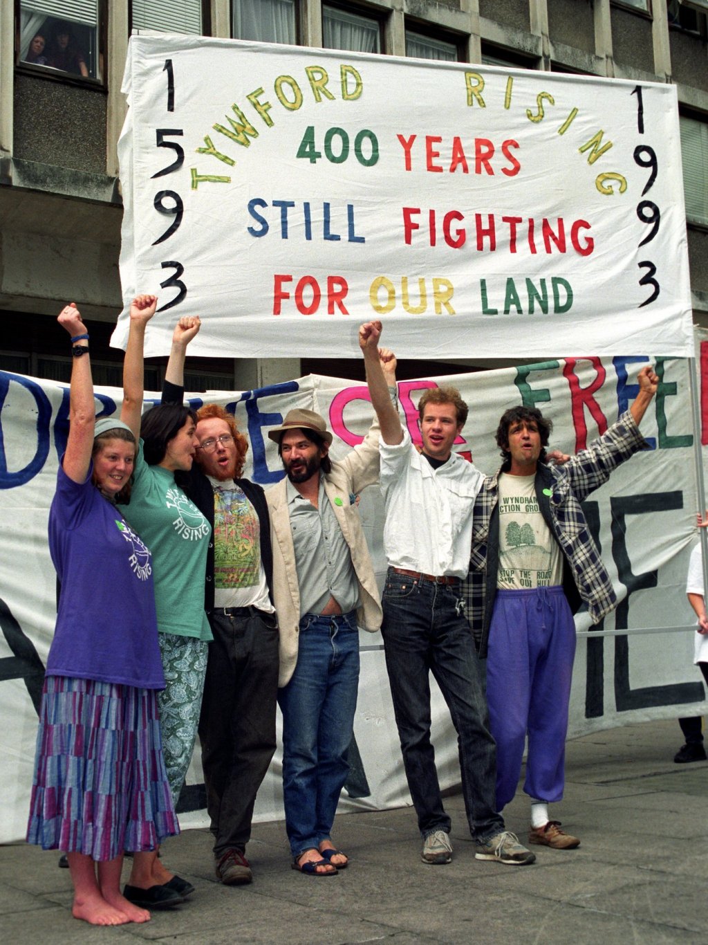 Seven people raise triumphant fists under a banner reading 'Twyford Rising: 400 years. Still fighting for our land'